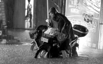 10日晚，广西柳州，一名市民在雨中推车通过积水路段。图/东方IC