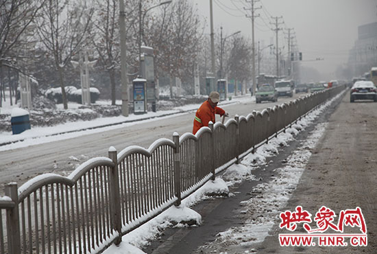 东风路上，一名环卫工人正在护栏旁清扫积雪